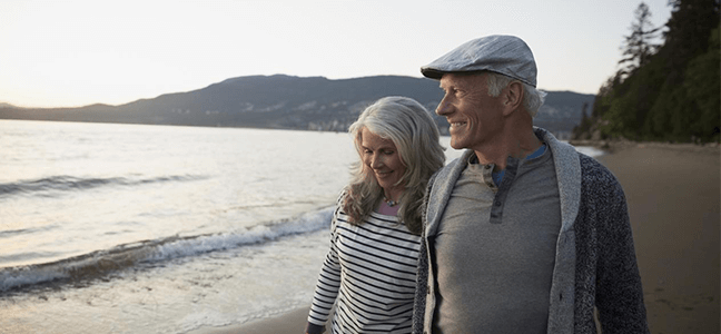 A mature-aged couple strolling along a beach, smiling into the sunset.