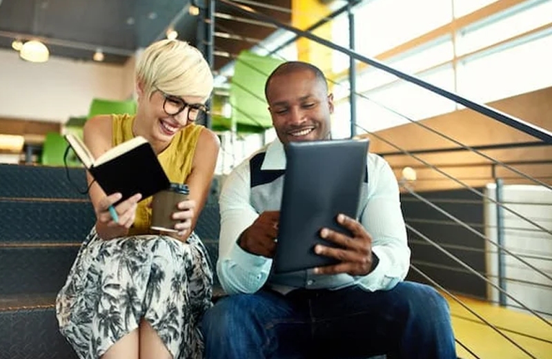 A man and woman smiling at an electronic tablet.