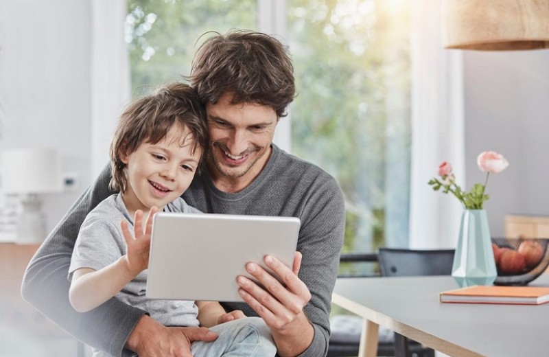 A father and a son smiling while interacting with a tablet